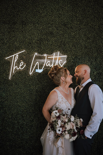 Wedding couple standing in front of green wall with neon sign leaning in for a kiss at Flores & Pine in Calgary