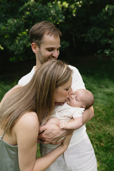 Foto van moeder die haar newborn baby een kus geeft. Vader houdt de baby vast.