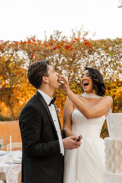 Bride laughing while she feeds a taste of wedding cake to her groom