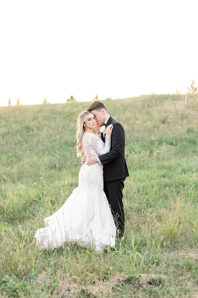Bride and Groom cuddled together at sunset in an open field.