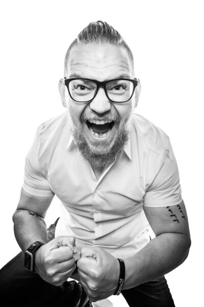 Editorial-style brand portrait of a man, cheering toward the camera in excitement. 