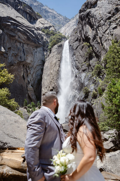 A newlywed couple with their arms around each other smiling at an overlook in Yosemite