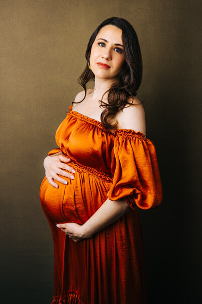 Maternity portrait of a woman in a black dress and denim jacket, leaning against a tree outside her Chestnut Hill home with her eyes closed.