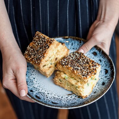 Baker holding a plate of gluten-free seeded pastries at Grain Artisan Bakery & Craft Coffee.