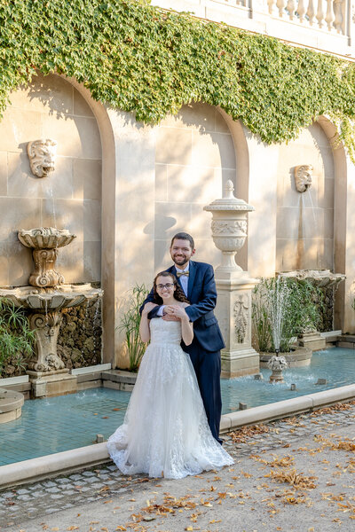 Elegant portrait of a bride and groom standing by a fountain in a historic Longwood Gardens in Kennett Square, Pennsylvania.