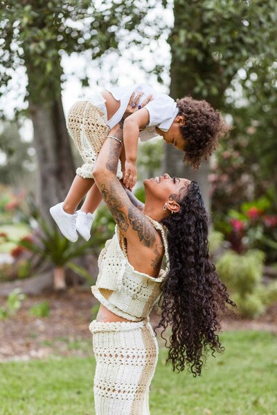 A mom lifting her toddler son up above her head playfully