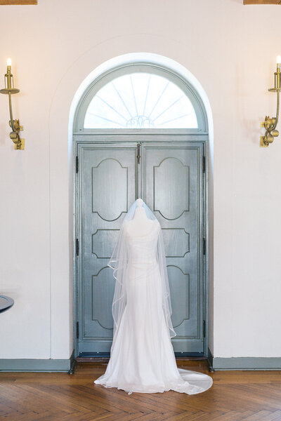 Wedding Dress on mannequin sits inside Crane Cottage in front of blue door.