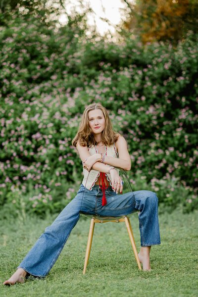 Senior girl in jeans and a croche top sitting in a chair in a pose with one  leg out and one leg bent