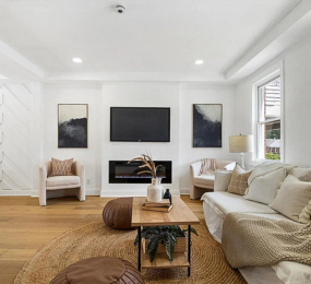 Beautifully renovated living room featuring a modern fireplace with wall-mounted TV, custom trim work, wide-plank hardwood floors, and natural light—designed for comfort and style.