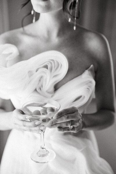 Bride in strapless sculptural gown holding a coupe glass during wedding celebration