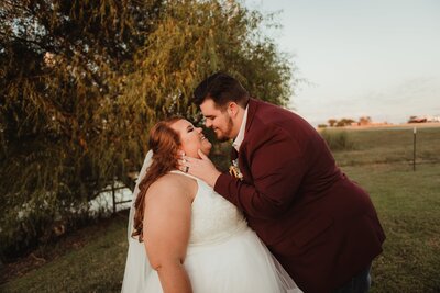 a bride and groom standing near a tree and fence line with cattle in the background at their Royse City wedding venue, Big Sky. Capture by Shelly Voss