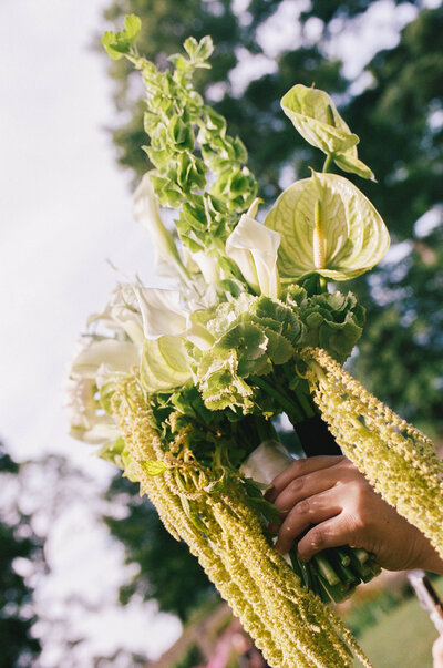 film photo of bride holds green and white bridal bouquet up to the sun taken by boston documentary wedding photographer