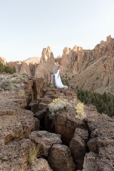 Groom dipping bride on side of cliff in Smith Rock State Park in Oregon.