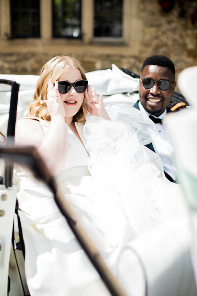 white bride and black groom wearing sunglasses in a beetle car