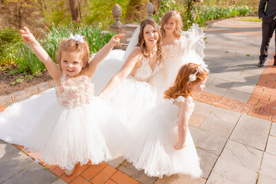 A bride and her flower girls dance around in joy and Gramercy Mansion Wedding Photographer snaps a photo