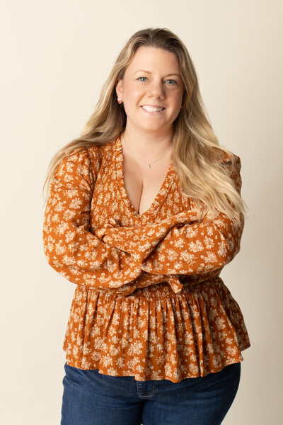 Kate McCord in an orange floral top with her arms crossed smiling in her Harrisburg photography studio