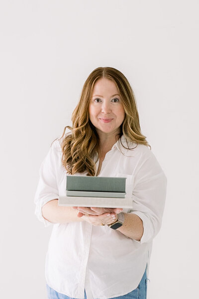 Self-portrait of woman with red hair wearing a white button down shirt holding heirloom albums. Tampa photographer