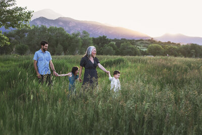 Family holding hands walking through tall grass with mountains