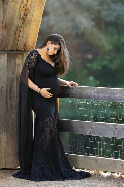 Long haired pregnant mother during maternity photos wearing looking at her baby in belly wearing long black gown