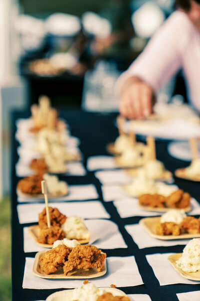 Close-up of individually plated fried chicken and mashed potatoes arranged on a black tablecloth, captured by Joseph Mayden during an outdoor event photography session.