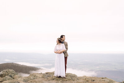 Bride and groom standing hand in hand with a mountain lake behind them during their intimate Virginia elopement, photographed in natural light and soft tones.

