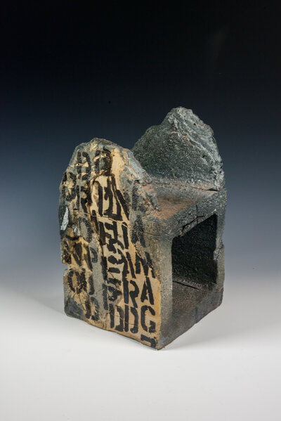 A cinder block that was hand made out of clay is decorated with underglaze to resemble graffiti and various other imagery