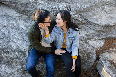 Bride to be in jeans and mustard blouse with jean jacket embraces groom in jeans and tan shirt with green jacket in the mountains of NC for their asheville engagement photography