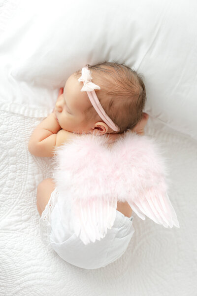 newborn baby girl on her belly with wings on her back. 