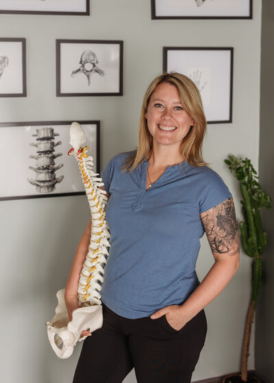 Chiropractor Brittany Fisk holding a spine model and smiling inside her chiropractic office.