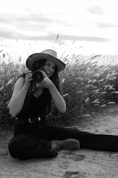 woman wearing a cowboy hat in a field holding a camera