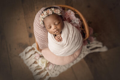 newborn girl wrapped in pink placed on boho style bamboo chair in niagara, on newborn photography studio