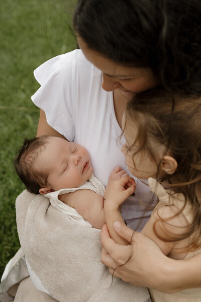 Mom and new big sister holding newborn baby boy in cream colored blanket during in home newborn session with Alexis Adkins Photography in Erie Colorado