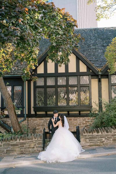 Bride and groom embracing near heritage building facade at Old Mill, romantic wedding photo in Toronto