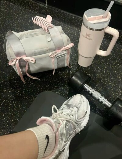 Girl's foot wearing tennis shoes, a gym bag with hair clip attached, gallon size Stanley cup and small weight