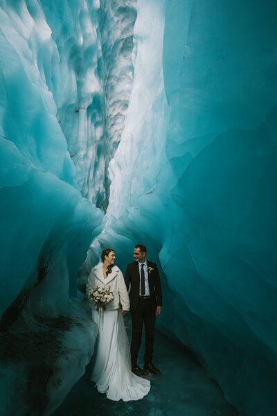 bride and groom standing in a glacier cave towering above them during their alaska helicopter elopement
