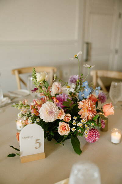 Intimate wedding reception decor showcasing elegant floral centerpieces with ivory roses, greenery, and candles by Leigh Florist.