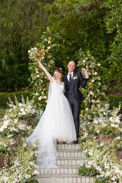 Bride and groom stand in front of a whimsical white ceremony arch installation at Newhall  Mansion