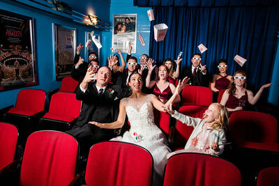 Newlyweds with their wedding party in a small theater throwing popcorn containers