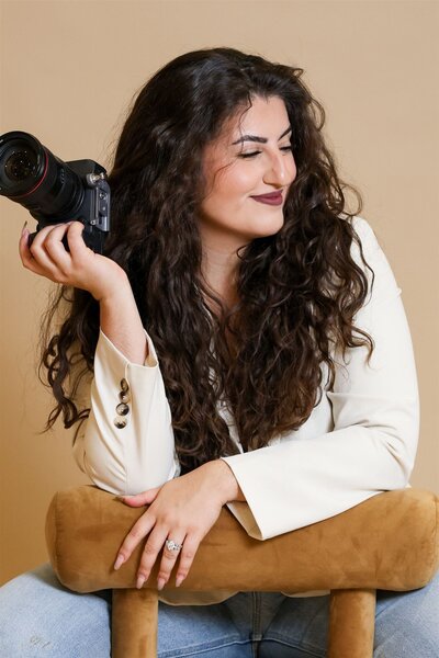 Portrait of Hiba, Raleigh-based photographer and filmmaker, smiling and holding camera during studio branding photoshoot.