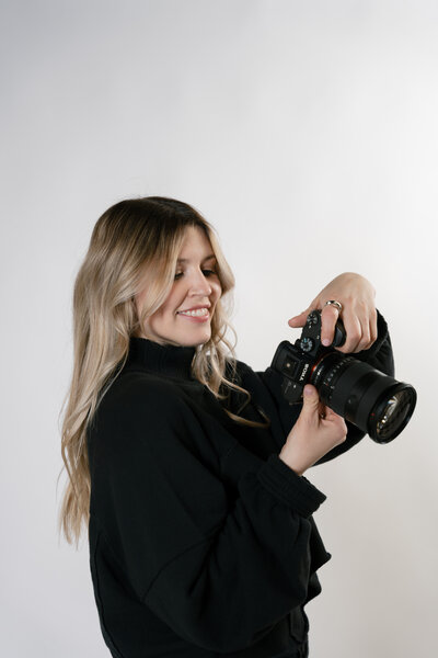 Photo of a photographer holding a camera in a studio with a white backdrop
