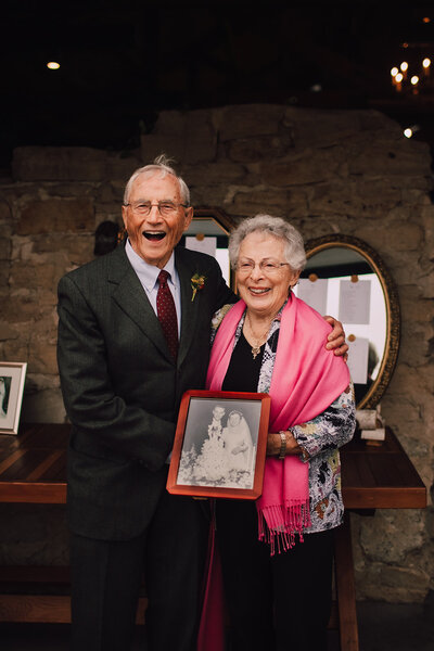 An elderly couple holds their wedding photo