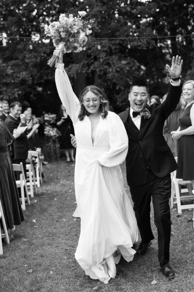 black and white photograph by bauer creative of bride and groom jovially walking down the aisle together at the end of their minneapolis wedding ceremony