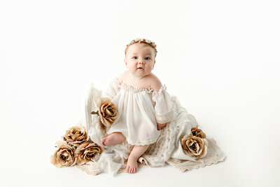 6 month old baby girl sitting on small doll bed adorned with neutral flowers. Neutral, vintage, classic, artistic, sitter session with fresno photographer, one good shot photography