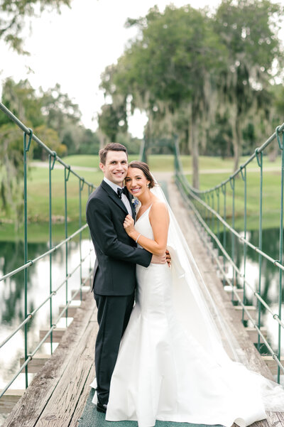 Bride and groom hugging on bridge with mossy trees at Lakeside Country Club in Houston