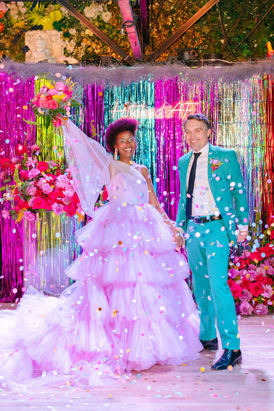 A bride and groom in colorful outfits smiling.