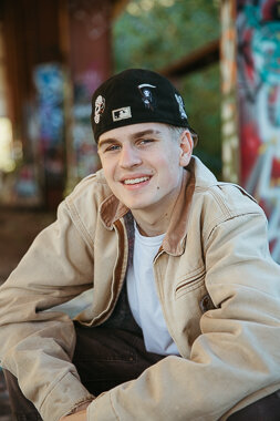 Graduating senior boy with a large jacket and graffiti walls in the background