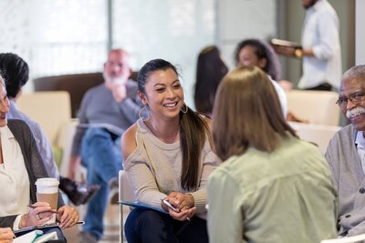 Smiling woman engaged in leadership coaching conversation in a group setting.
