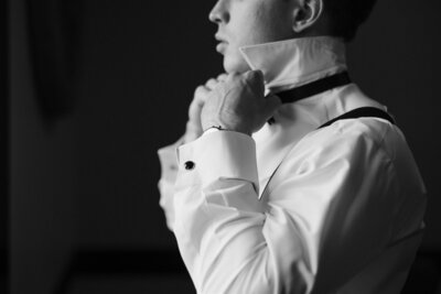 Groom puts on his bow tie as he gets ready for his wedding