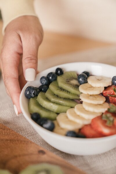 A hand with beige nail polish holding a bowl of fruit.