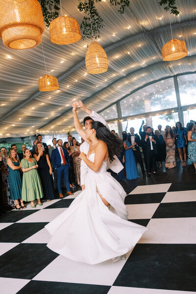Groom twirls bride beneath wicker lanterns on checkboard dance floor at Glen Foerd Estate in Philadelphia, PA